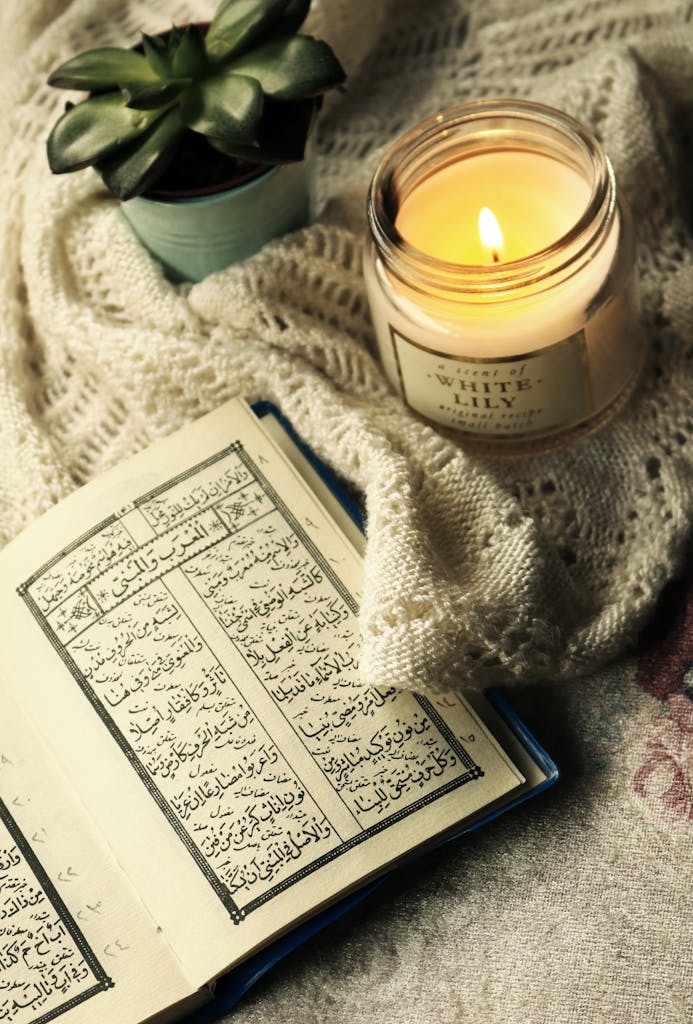 Quran Tafseer Online Classes 1 An inviting scene featuring an open Quran, a burning candle, and a houseplant on a cozy fabric.