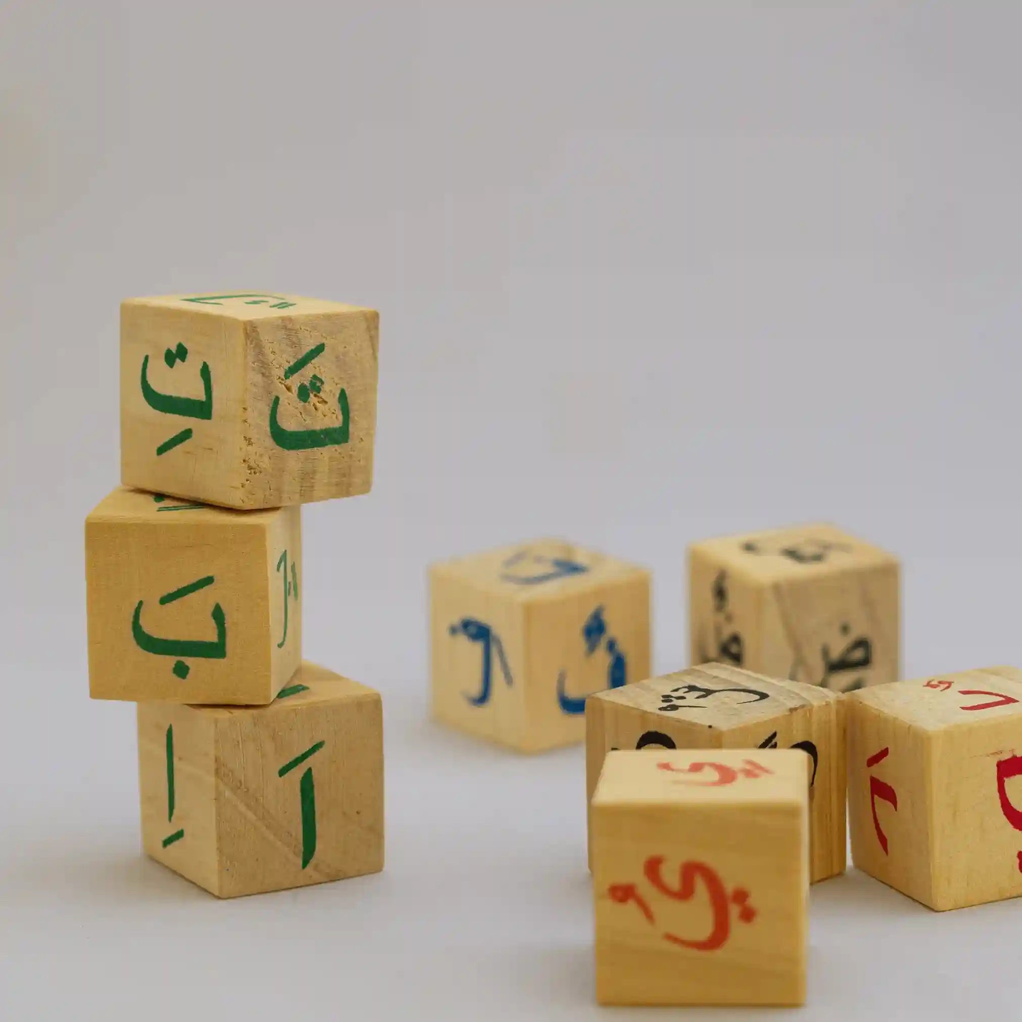 Wooden toy blocks with red and green Arabic letters scattered on a white surface