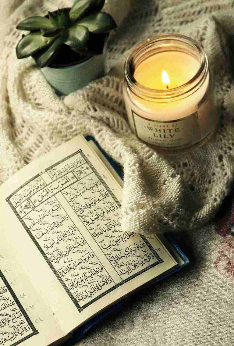 Open Quran beside a lit candle and houseplant on soft cozy fabric