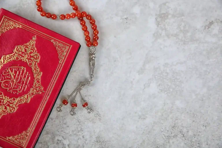 How to Memorize the Quran: Proven Methods, Daily Schedules, and Expert Tips for All Ages 8 Red Holy Quran with red tasbeeh prayer beads placed on a light stone background, representing Islamic faith, Quran recitation, and spiritual reflection.
