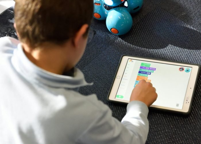 STEM Learning for Kids – Coding with Robotics & Visual Programming A young child using a tablet for block-based coding with a blue educational robot in the background, promoting STEM and early childhood programming education.